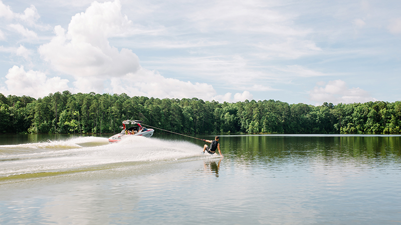 Wake boarder riding across a lake behind a speed boat on a lake.